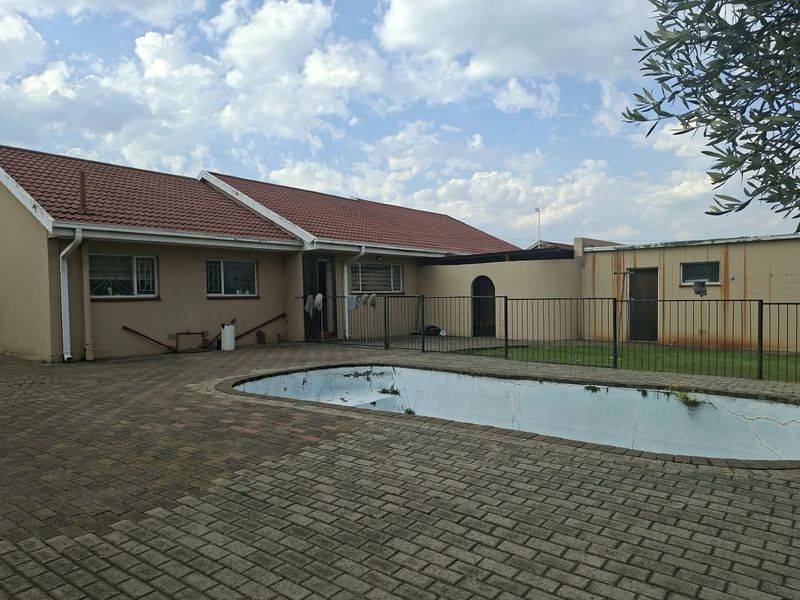 Rear exterior view featuring a paved patio area and a swimming pool requiring maintenance, set against the back facade of the house.