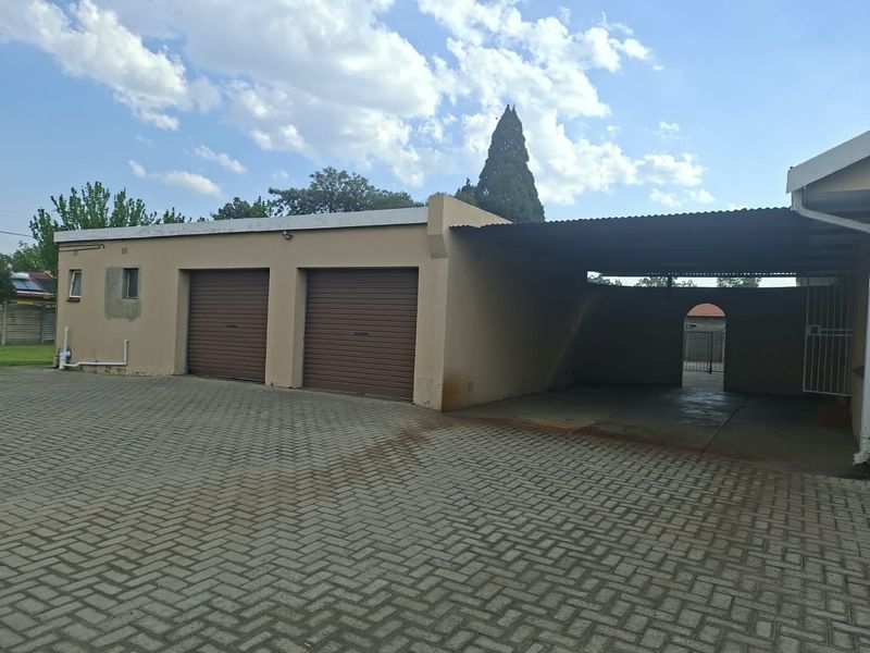 A detached garage structure featuring two roller doors and an adjacent covered carport, set on a paved driveway area.