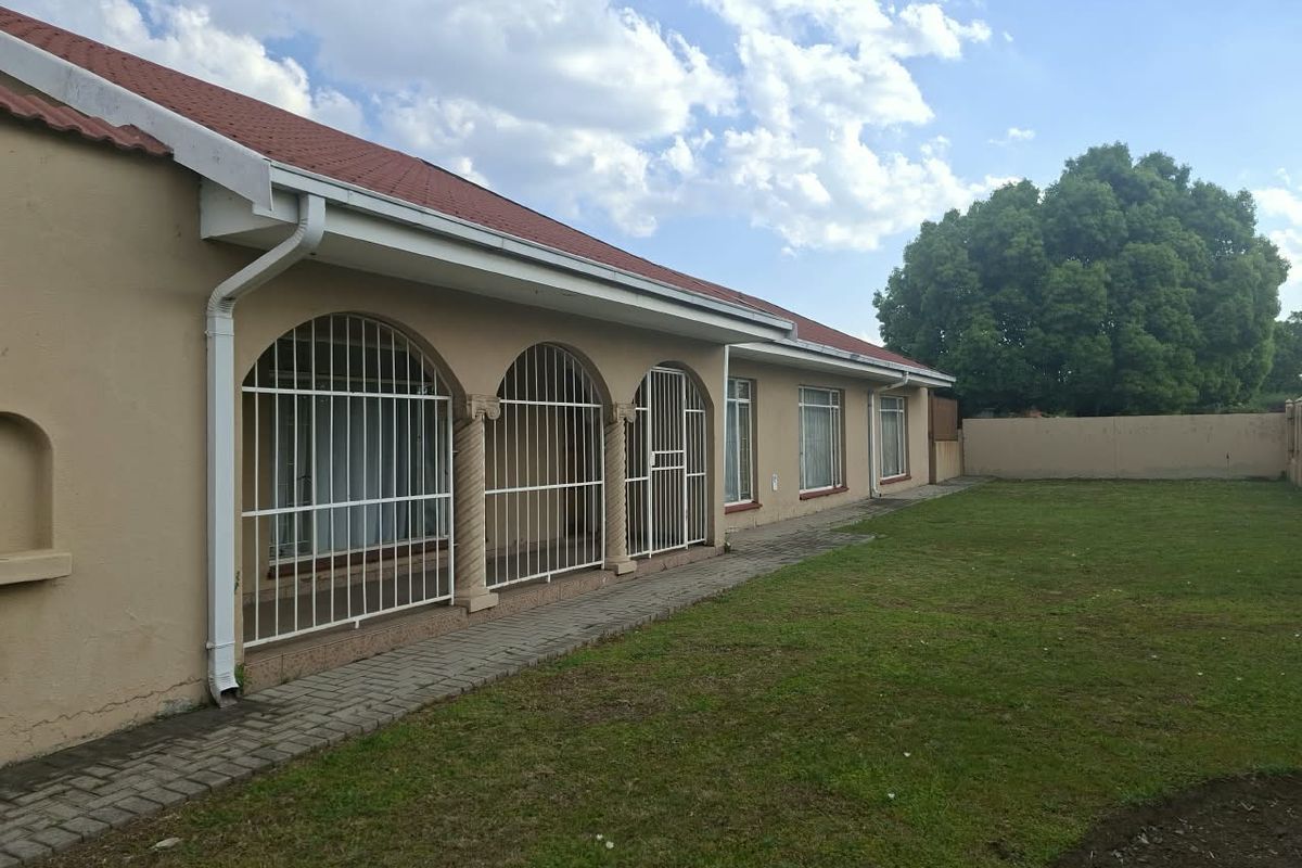 Rear view of the house featuring a paved walkway, security-barred arched windows, and a spacious garden area with a perimeter wall.