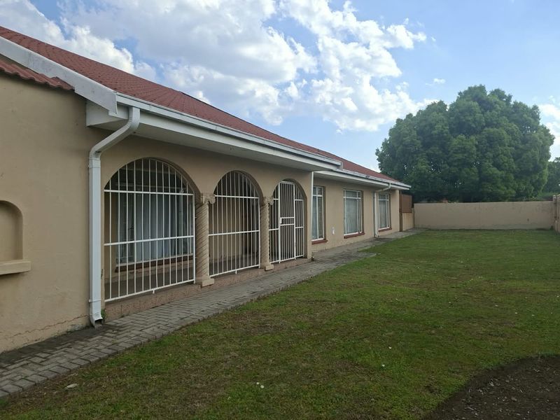 Rear view of the house featuring a paved walkway, security-barred arched windows, and a spacious garden area with a perimeter wall.