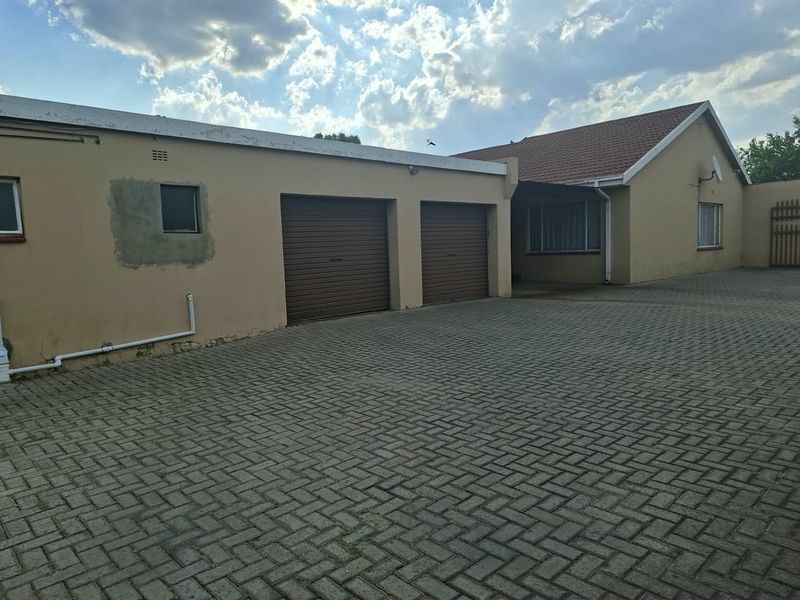 Front exterior view of the property featuring a double garage with roller shutter doors and an extensive paved driveway area.