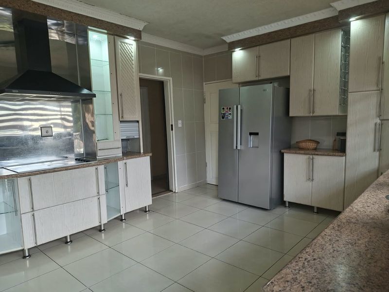 A functional kitchen featuring light wood-grain cabinetry, granite countertops, tiled walls and floors, and a stainless steel extractor fan.