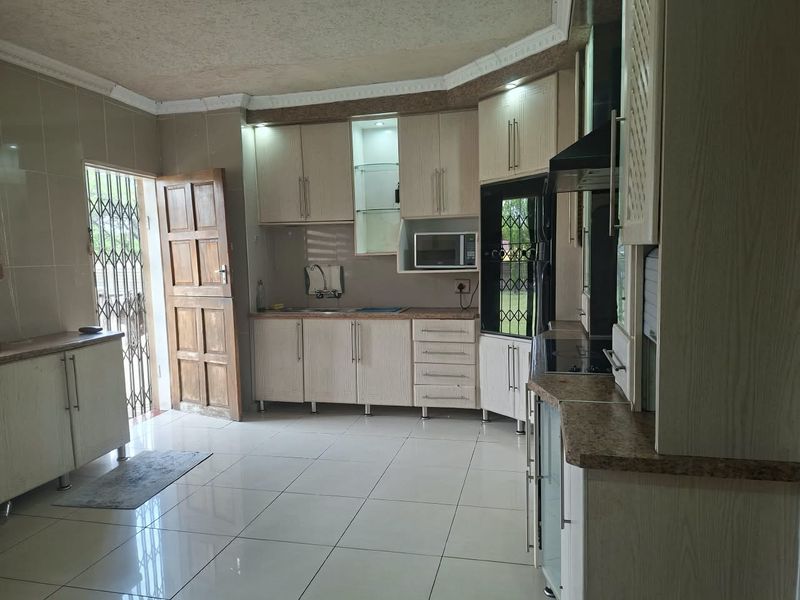 A functional kitchen featuring light-toned built-in cabinetry, laminate countertops, and tiled flooring, with direct access to an exterior security gate.
