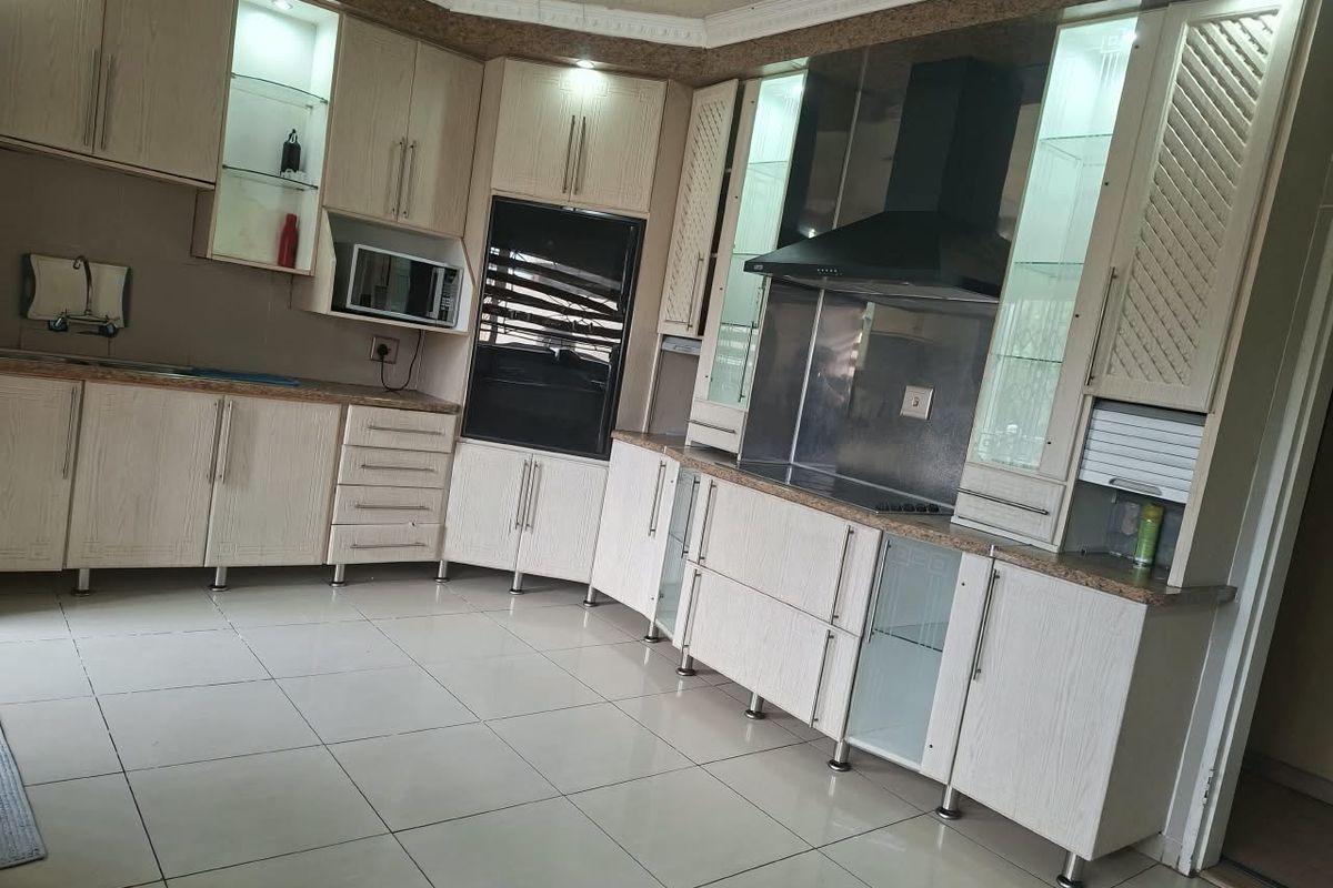 A well-appointed kitchen featuring light wood-grain cabinetry, granite countertops, integrated appliances including an oven and extractor fan, and tiled flooring.