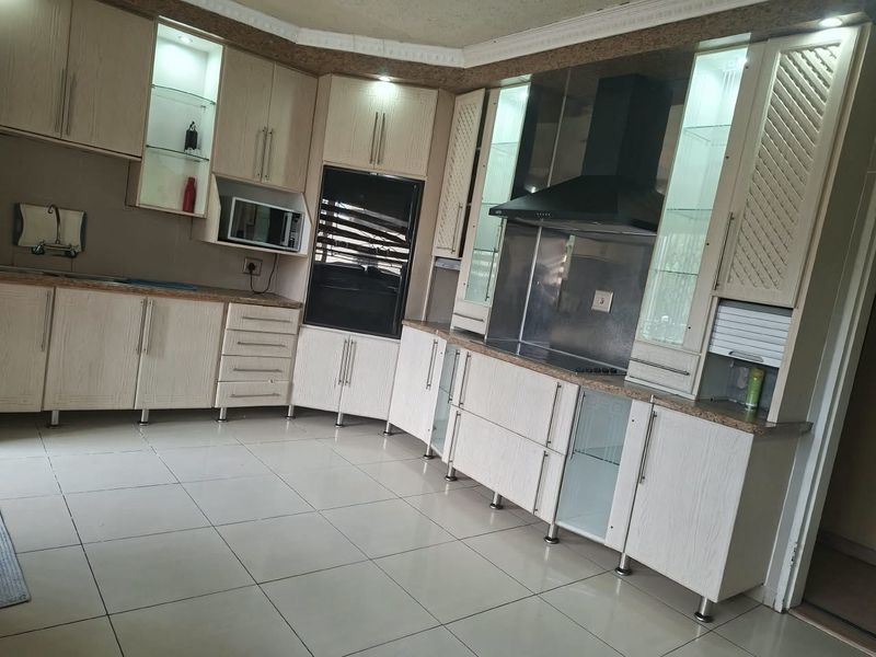 A well-appointed kitchen featuring light wood-grain cabinetry, granite countertops, integrated appliances including an oven and extractor fan, and tiled flooring.