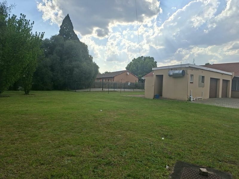 A spacious rear garden area featuring a large lawn, paved driveway, and access to the garage and exterior utility area.