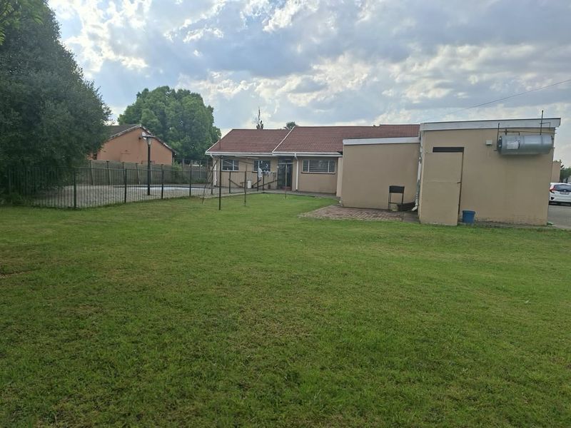 Rear view of the property featuring a spacious lawn, paved patio area, perimeter fencing, and an external geyser mounted on the wall.