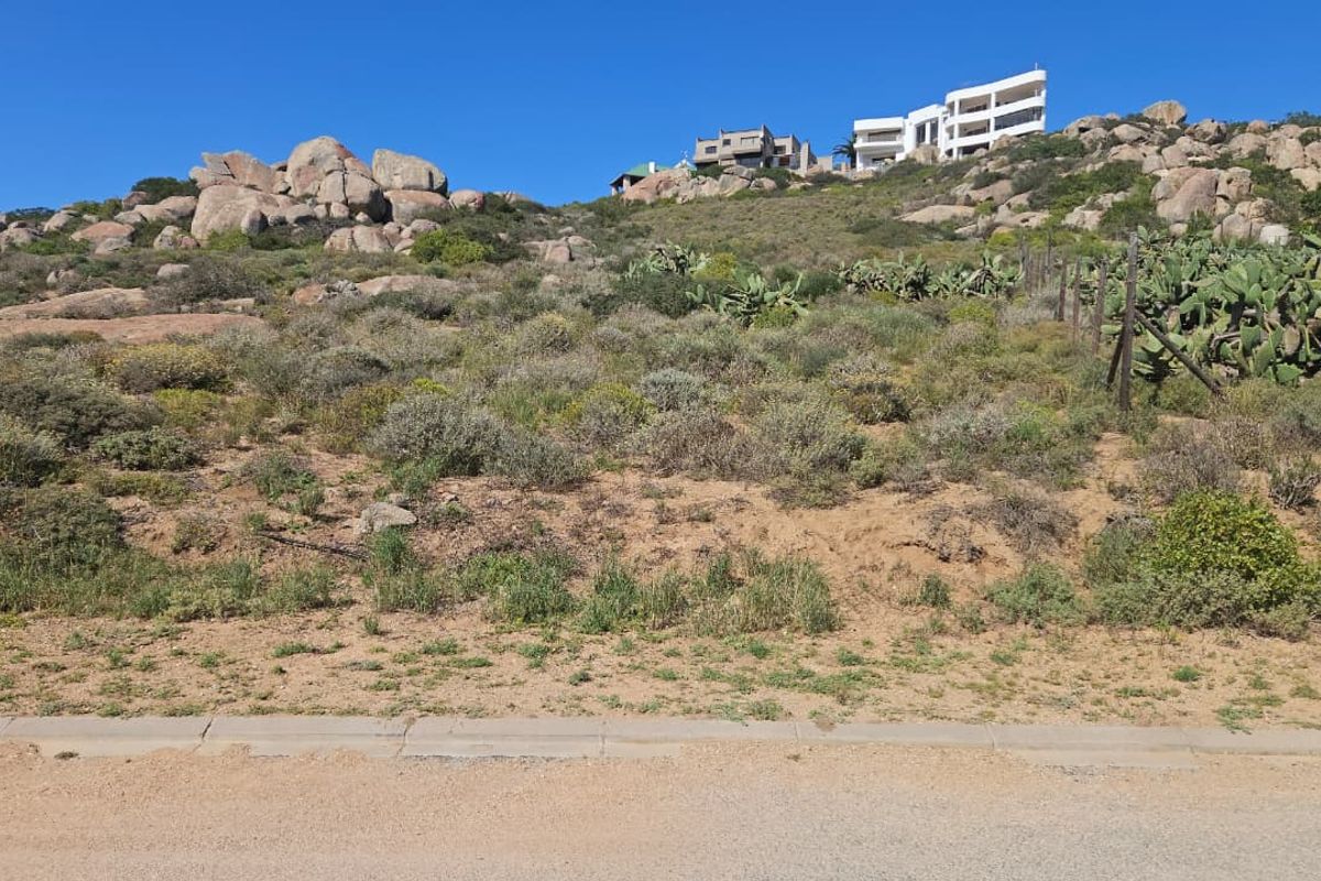 A sloped residential vacant land plot featuring natural rocky terrain and indigenous vegetation, offering an elevated position with surrounding hillside views.