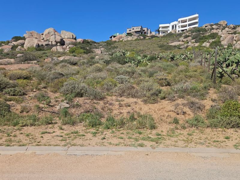 A sloped residential vacant land plot featuring natural rocky terrain and indigenous vegetation, offering an elevated position with surrounding hillside views.