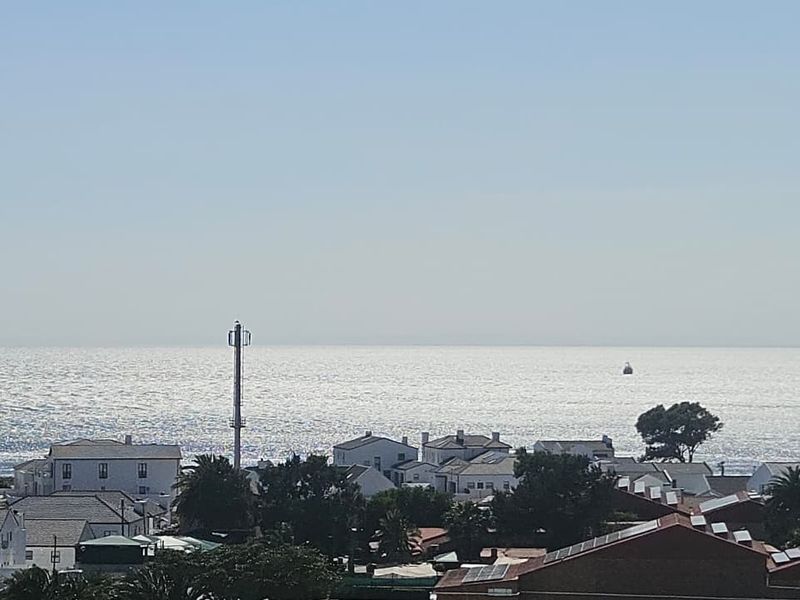 An elevated coastal view overlooking residential rooftops and the ocean horizon, featuring a prominent telecommunications tower in the foreground.