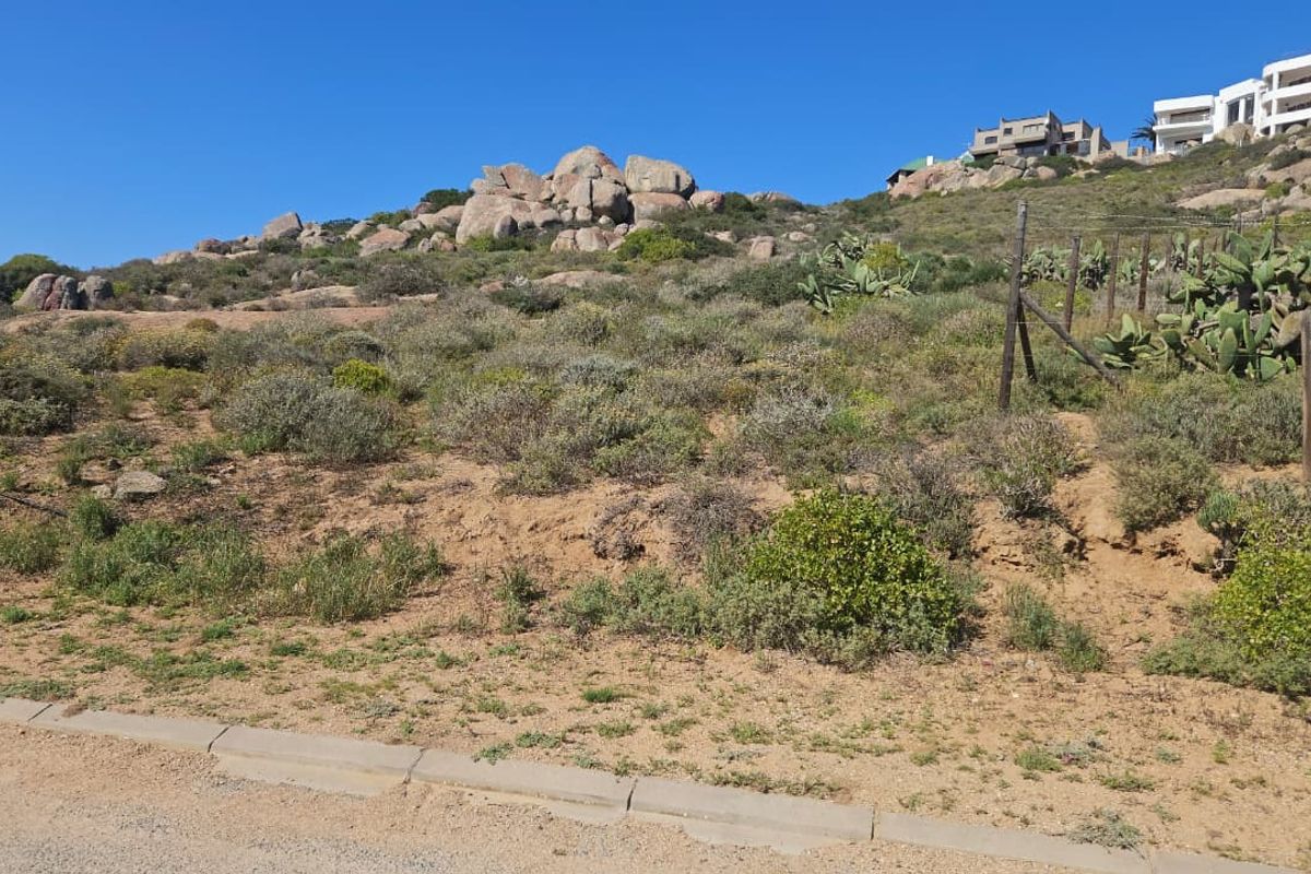 A vacant residential plot featuring natural rocky terrain, indigenous vegetation, and existing boundary fencing, offering potential for development in a scenic hillside location.