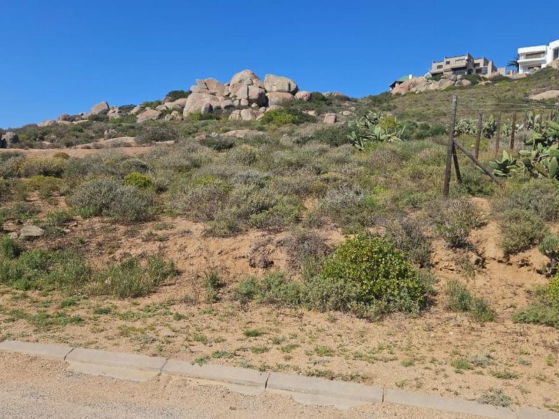 A vacant residential plot featuring natural rocky terrain, indigenous vegetation, and existing boundary fencing, offering potential for development in a scenic hillside location.