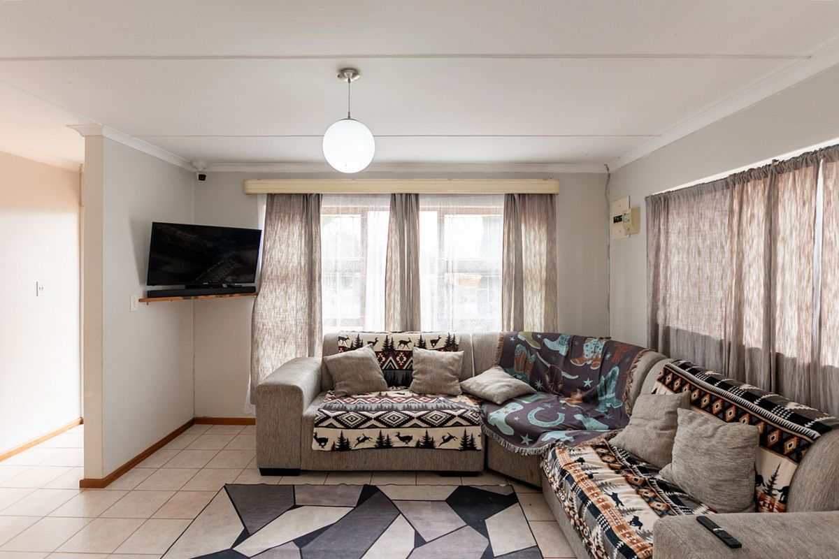 A comfortable living room featuring tiled flooring, neutral walls, and natural light through large windows with curtain rails.
