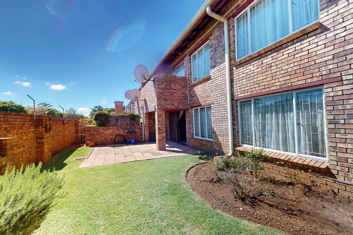 Rear view of the townhouse featuring a paved patio, built-in brick braai, and a private garden area with perimeter brick walling.