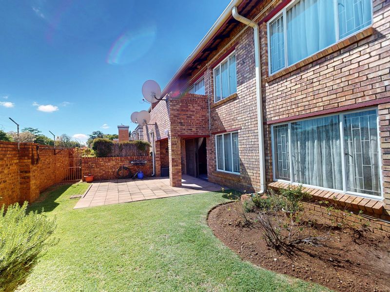 Rear view of the townhouse featuring a paved patio, built-in brick braai, and a private garden area with perimeter brick walling.