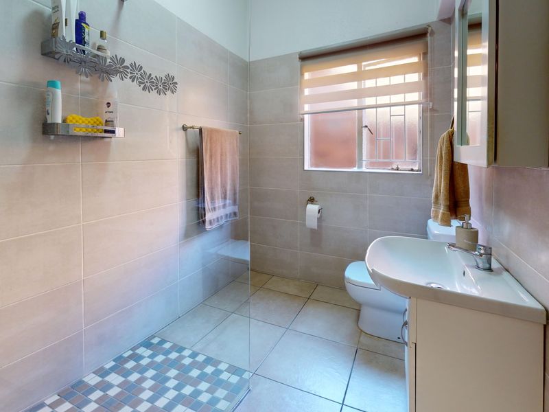 A well-maintained bathroom featuring a walk-in shower with a glass screen, tiled finishes, a vanity basin, and a toilet.