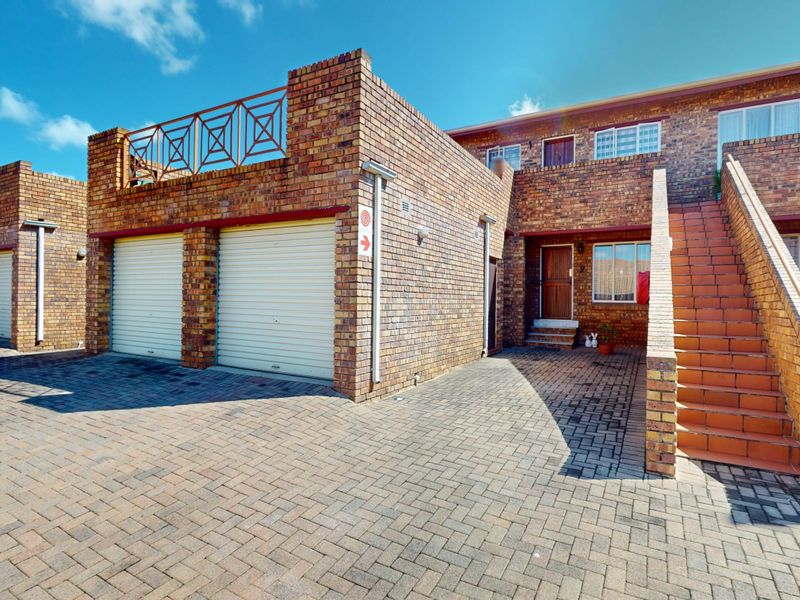 Front exterior view of a face brick townhouse complex featuring a double garage, paved driveway, and an external staircase leading to upper levels.