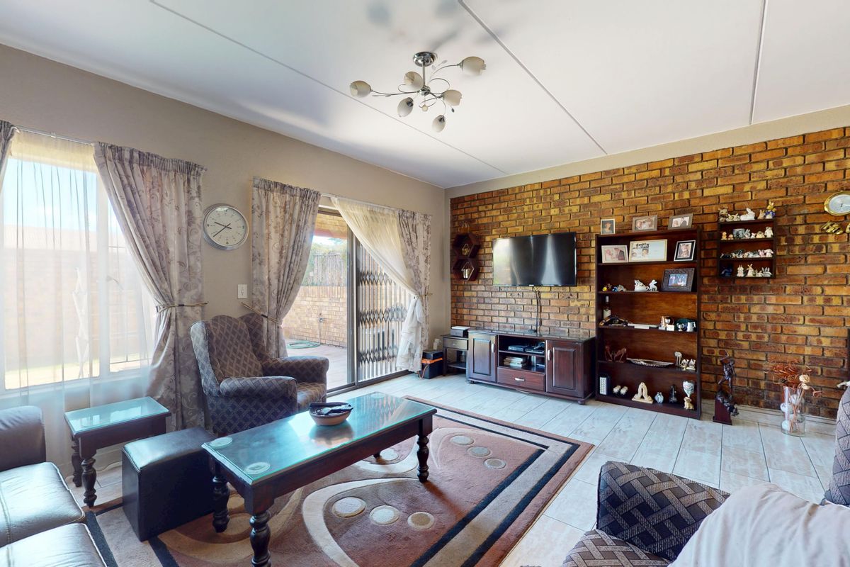 Spacious living room featuring an exposed brick accent wall, tiled flooring, and a sliding glass door providing access to the outdoor area.