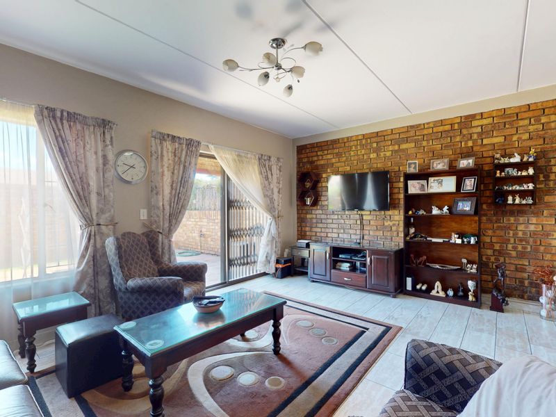 Spacious living room featuring an exposed brick accent wall, tiled flooring, and a sliding glass door providing access to the outdoor area.