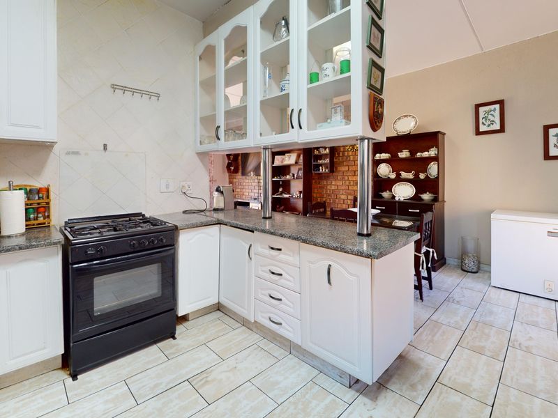 A functional kitchen featuring white cabinetry, granite countertops, a gas stove, and tiled flooring, with an open-plan layout connecting to the dining area.