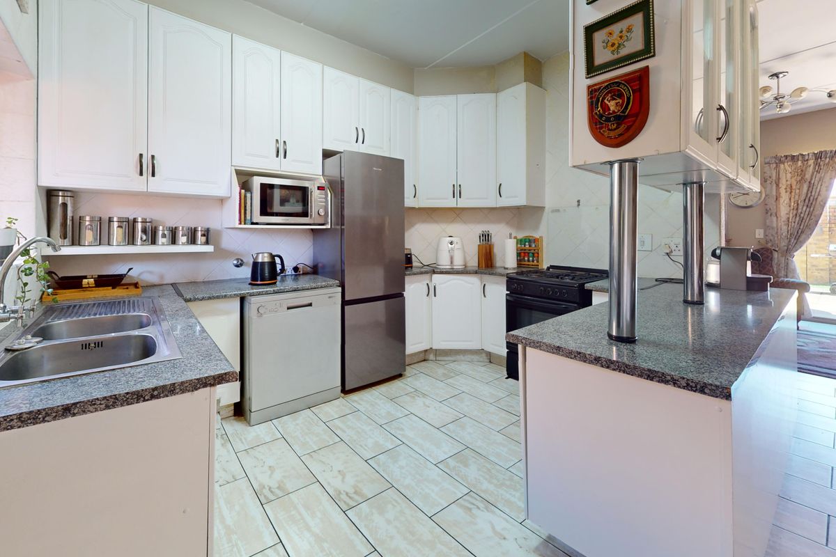 Functional kitchen featuring white cabinetry, granite countertops, double sink, and a breakfast bar, with direct access to the outdoor area.