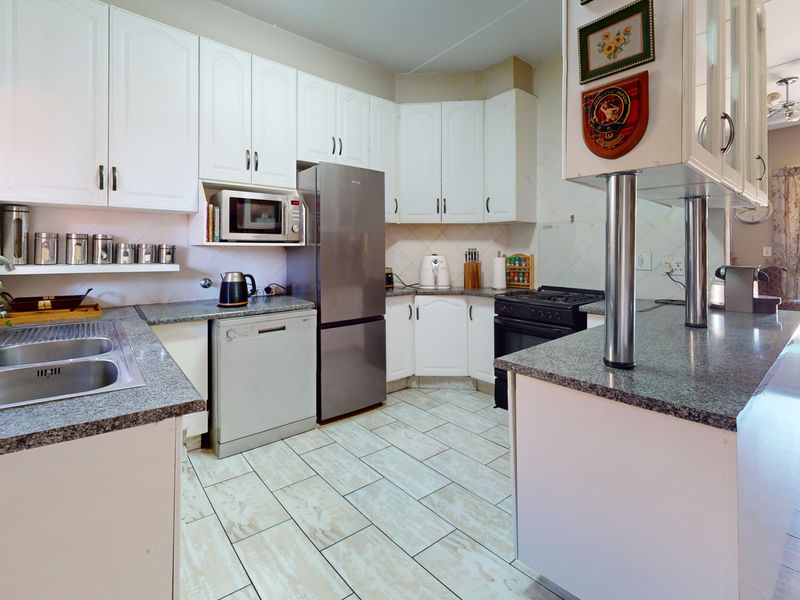 Functional kitchen featuring white cabinetry, granite countertops, double sink, and a breakfast bar, with direct access to the outdoor area.