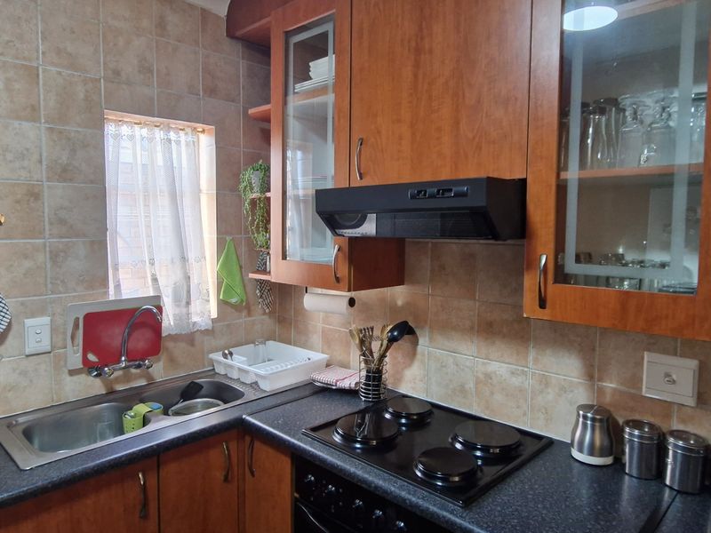 A functional kitchen featuring wood-finish cabinetry, dark laminate countertops, a built-in electric hob with extractor fan, and tiled splashbacks.