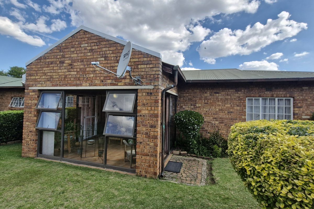 Rear view of a face brick townhouse featuring a sunroom with aluminium windows, a metal roof, and a small paved garden path.
