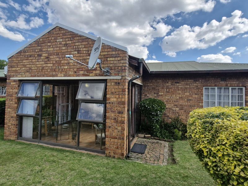Rear view of a face brick townhouse featuring a sunroom with aluminium windows, a metal roof, and a small paved garden path.