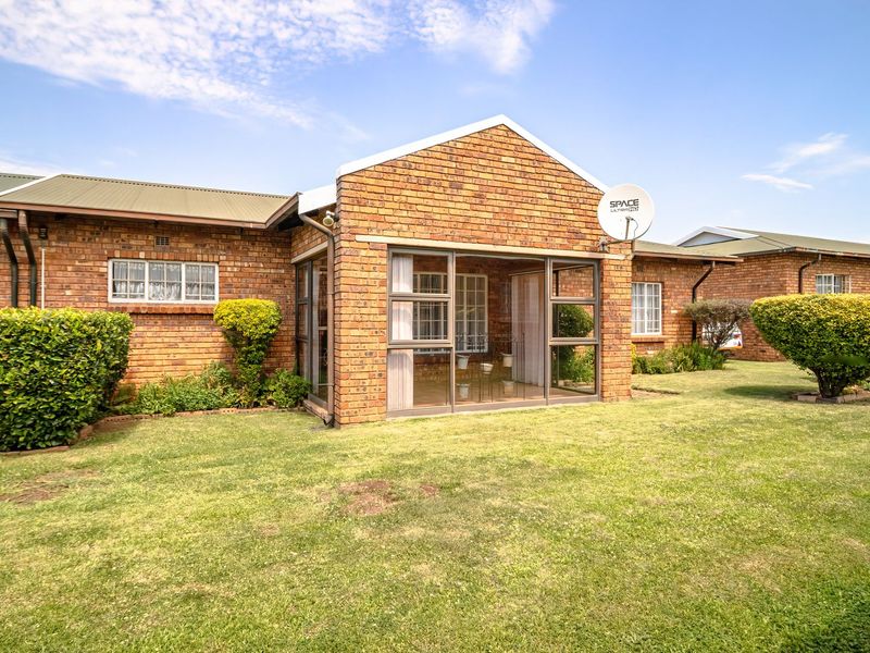 Rear view of a face brick townhouse featuring an enclosed patio area, well-maintained lawn, and established garden shrubs.