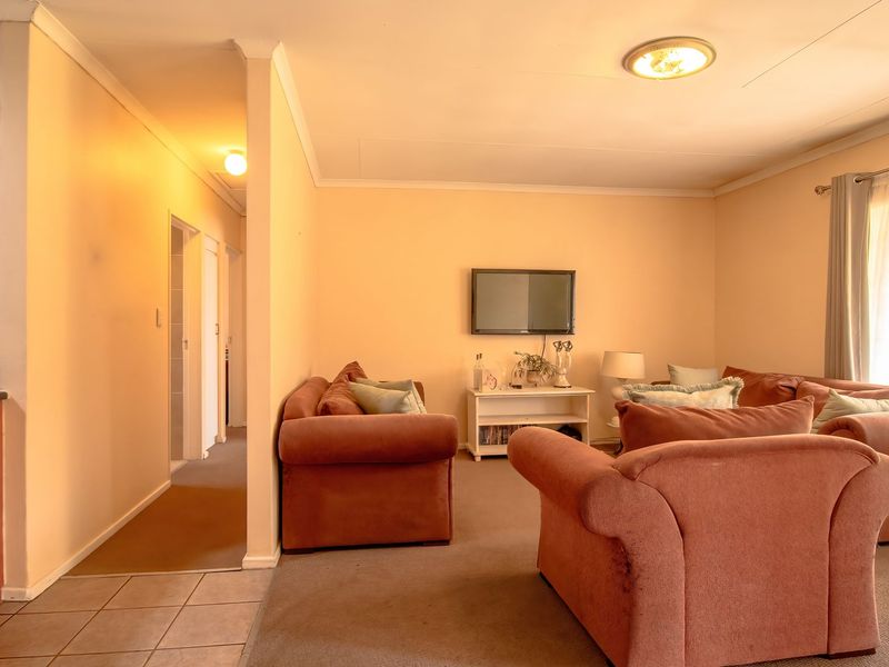 Open-plan living area featuring a compact kitchen with built-in cabinetry and a spacious lounge area with carpeted flooring.