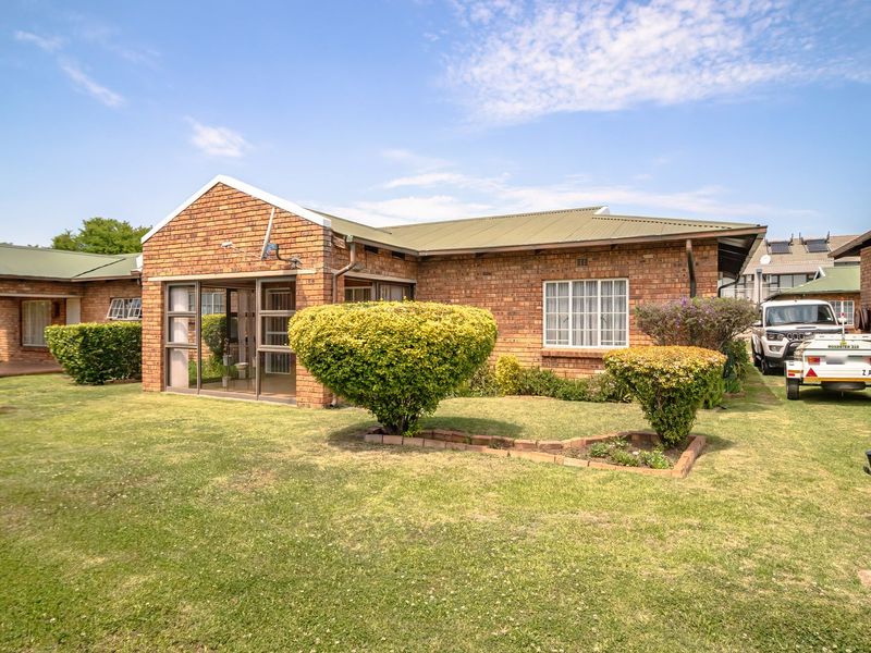 Rear view of a face brick townhouse featuring a covered patio with a built-in braai, sliding glass doors, and a well-maintained garden.