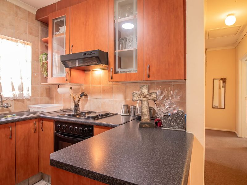 A functional kitchen featuring wood-finish cabinetry, dark laminate countertops, a built-in oven with hob, and tiled backsplash, adjacent to a carpeted hallway.