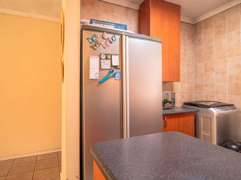 A functional kitchen area featuring laminate cabinetry, tiled splashbacks, and durable tiled flooring, offering a practical layout for daily meal preparation.