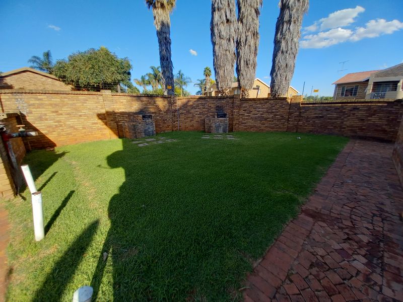 A private rear garden featuring a well-maintained lawn, brick boundary walls, and a built-in braai area with paved access.