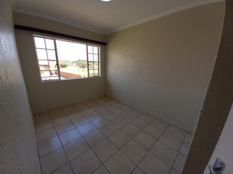 A bright, empty bedroom featuring neutral tiled flooring, textured walls, and a large window providing natural light.