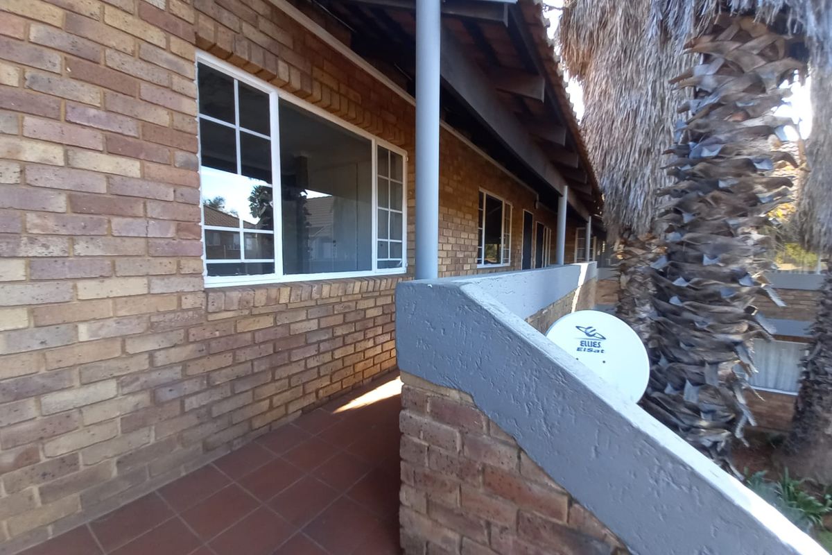 A view of the exterior rear walkway featuring face brick walls, a tiled floor, and a painted brick balustrade with a mounted satellite dish.