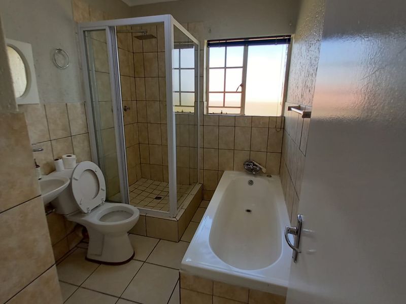 A functional bathroom featuring a separate shower enclosure, bathtub, toilet, and washbasin with neutral wall and floor tiling.