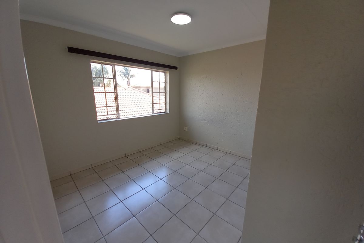 A clean, empty bedroom featuring neutral tiled flooring, a window with security bars, and a simple ceiling light fixture.
