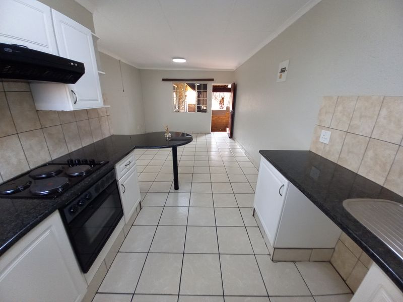 A functional kitchen featuring white cabinetry, granite countertops, a built-in oven with hob, and tiled flooring, leading into an open-plan living area.