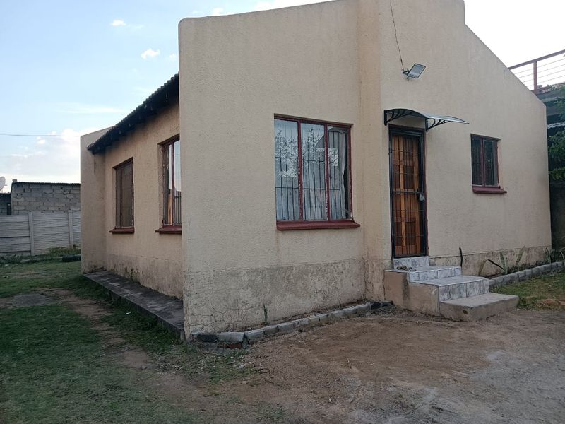 Front exterior view of a single-story house featuring plastered walls, security bars on windows, and a small tiled entrance area.