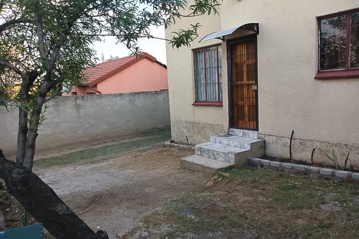 Rear exterior view of the house featuring a tiled entrance step, security gate, and boundary wall with visible signs of exterior wall wear.