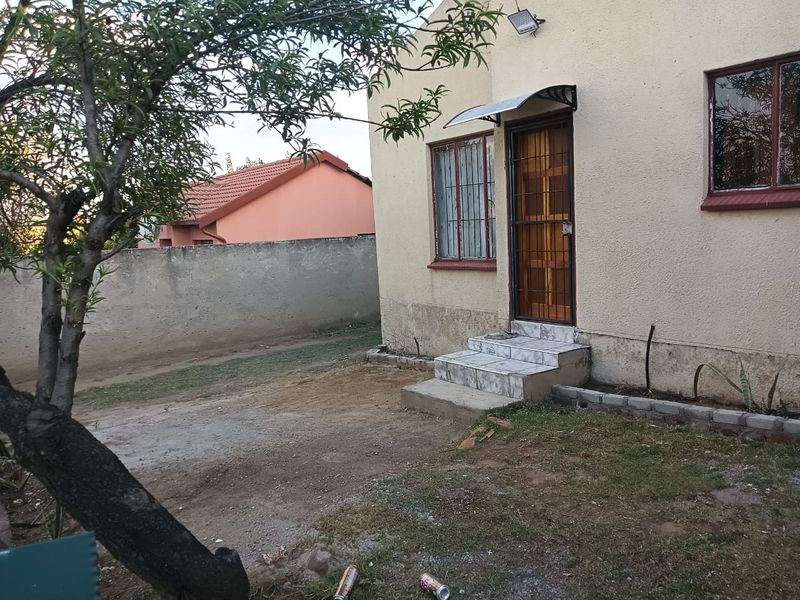 Rear exterior view of the house featuring a tiled entrance step, security gate, and boundary wall with visible signs of exterior wall wear.