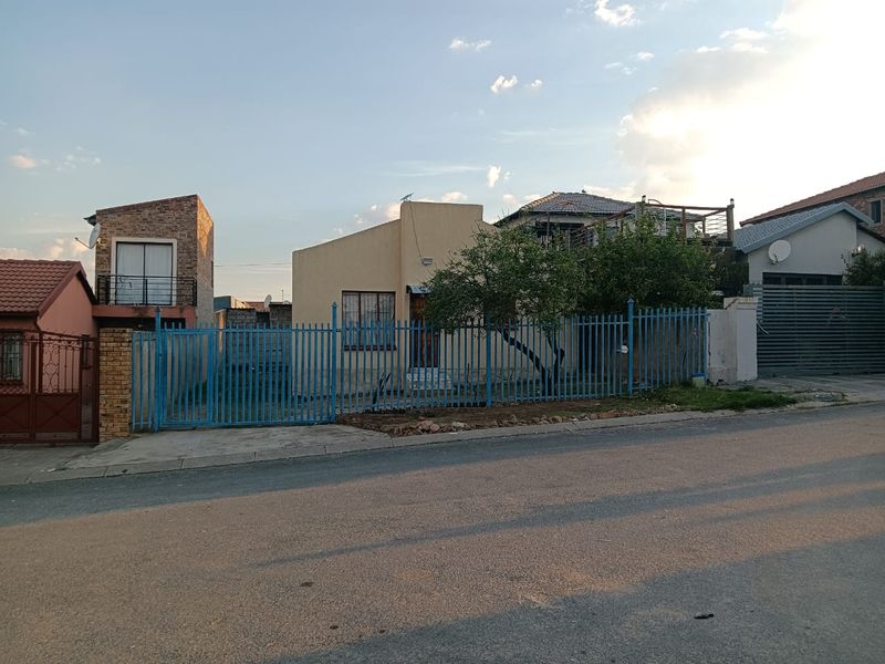 Front view of a residential property featuring a steel security fence, gated entrance, and paved driveway area.