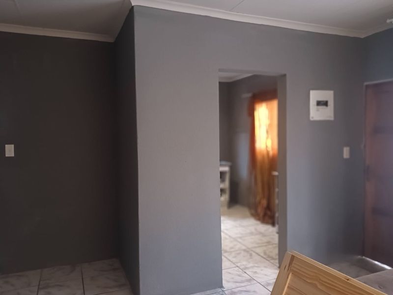An empty living area featuring grey painted walls, tiled flooring, and a doorway leading to an adjacent room.
