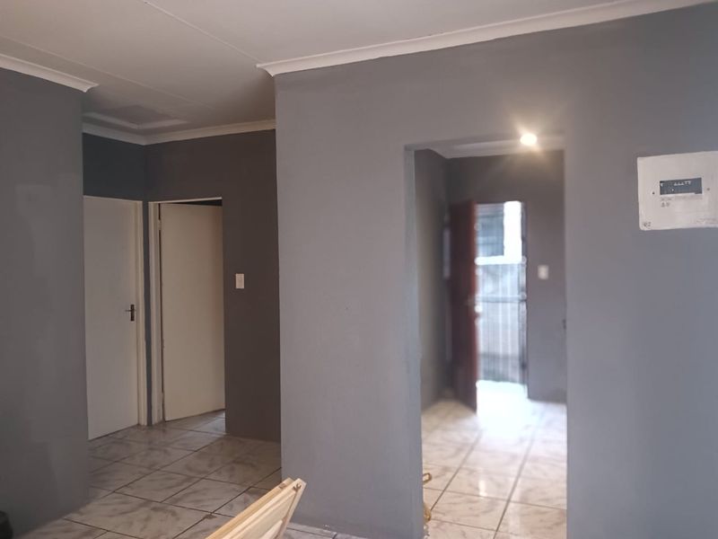 A neutral-toned hallway featuring tiled flooring, cove cornicing, and an accessible electrical distribution board, providing access to multiple rooms.