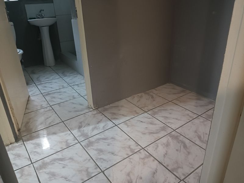 A small, empty bathroom featuring a pedestal basin and toilet with marble-effect ceramic floor tiles and unfinished wall surfaces.