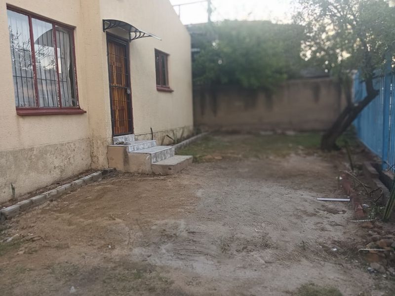 Rear exterior view of the property featuring a small tiled entrance, security gate, and an unlandscaped backyard area with perimeter walling.