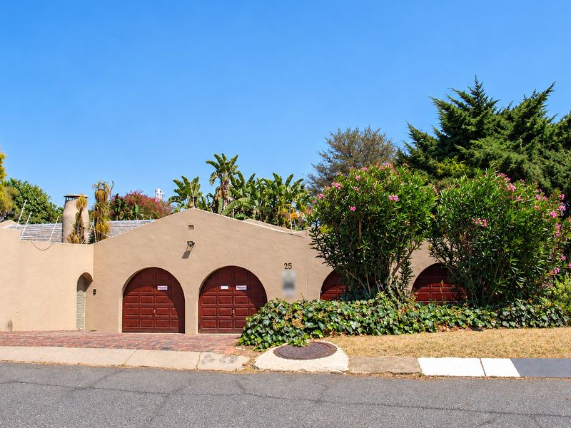 Front elevation of a residential property featuring a triple garage with arched wooden doors, paved driveway, and established garden landscaping.