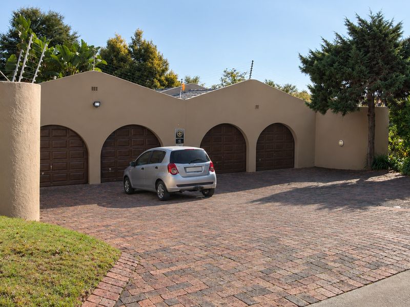 A spacious four-car garage featuring arched wooden doors, a paved driveway, and secure perimeter walling with electric fencing.